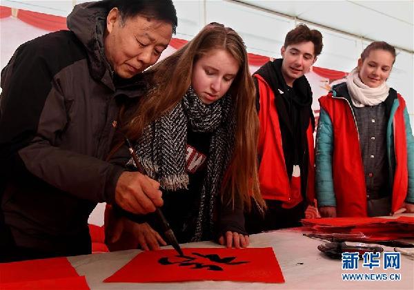 2月6日，来自德国的志愿者李米（左二）在书法爱好者的指导下学写“福”字，准备送给旅客。新华社记者李安摄